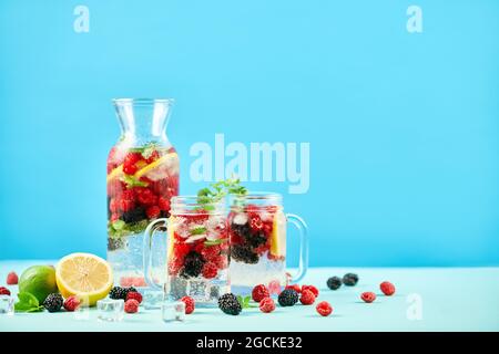 Fresh berries cocktails in glass jars and jug with copy space. Fresh summer cocktail with mix of berries, lemon and mint on blue background. Party, dr Stock Photo