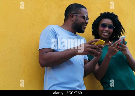 Black couple using a mobile phone leaning against a yellow wall Stock Photo