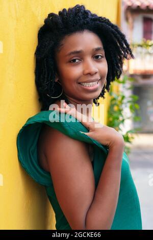 Close upside portrait of beautiful smiling young Black Woman leaning against wall outside Stock Photo