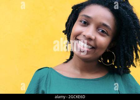 Close upside portrait of beautiful smiling young Black Woman leaning against wall outside Stock Photo