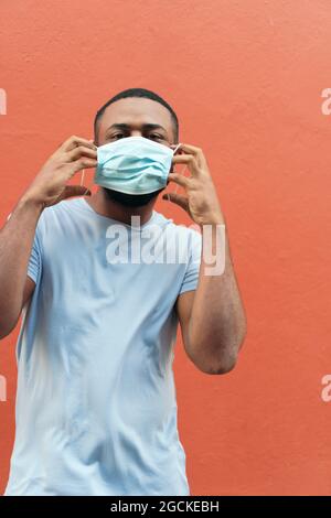 Portrait of a young man in front of a red wall wearing a medical mask to protect himself from the outbreak of the coronavirus, covid-19. Stock Photo
