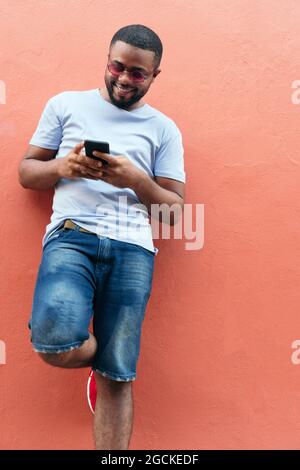 Smiling Black man looking at his smart phone while standing in the city Stock Photo