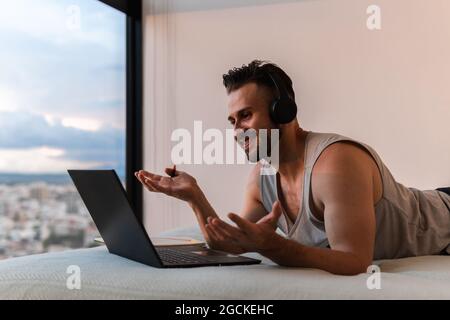 Side view of smiling male in headphones doing videoconference on netbook at home Stock Photo