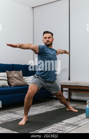 Concentrated athletic male doing stretch exercises near sofa while training at home and looking away Stock Photo