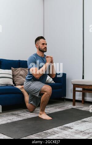 Concentrated athletic male doing lunge exercise near sofa while training at home and looking away Stock Photo