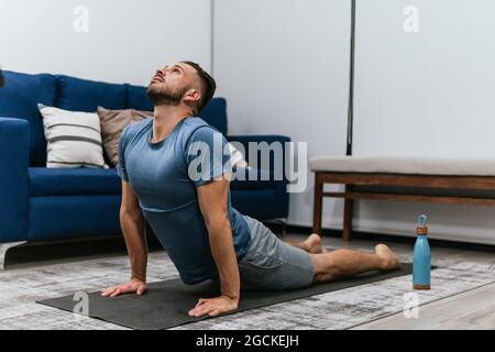 Flexible male in Bhujangasana doing yoga on mat and stretching body at home Stock Photo