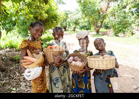 In this image, a group of pretty smiling African girls are carrying baskets full of vegetables, on their way to the lokal market Stock Photo