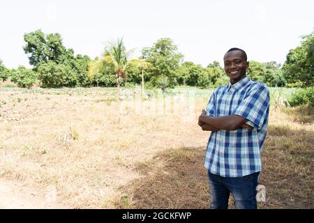 In this image, a content black African farmer is standing in front of a newly acquired, unplanted piece of land, intended for growing vegetables Stock Photo