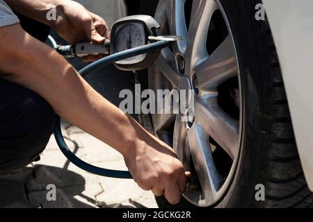 Close up mechanic inflating tire hand holding gauge pressure for checking and filling air in car tire. Automobile concept. Stock Photo