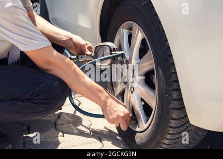 Close up mechanic inflating tire hand holding gauge pressure for checking and filling air in car tire. Automobile concept. Stock Photo