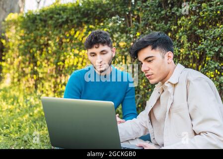 male colleagues browsing netbook and working on project remotely while sitting on lawn in park Stock Photo