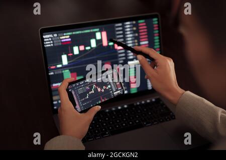 Faceless crop broker using mobile phone while working with financial chart during trading Stock Photo