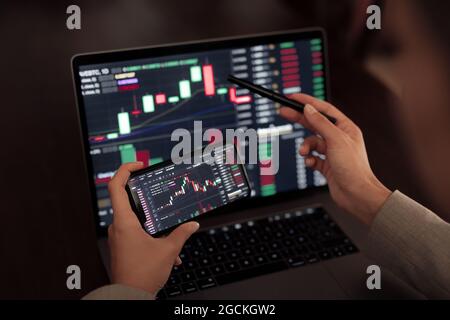 Faceless crop broker using mobile phone while working with financial chart during trading Stock Photo