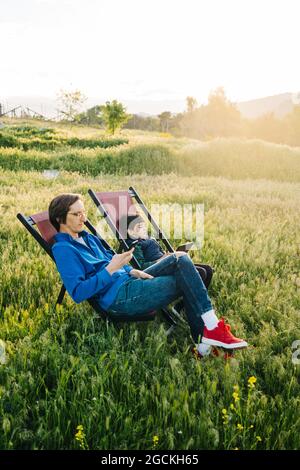 Side view of father and son relaxing in folding hammocks in the middle of the mountain at sunset Stock Photo