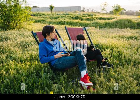 Side view of father and son relaxing in folding hammocks in the middle of the mountain at sunset Stock Photo