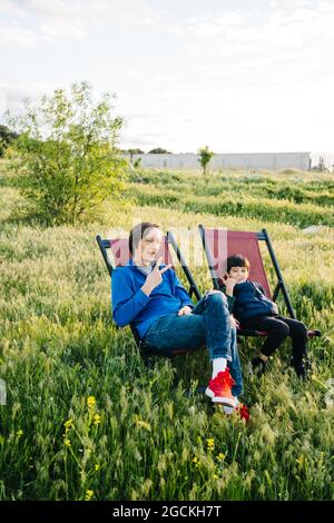 Side view of father and son relaxing in folding hammocks in the middle of the mountain at sunset Stock Photo