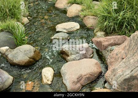 Water runs over the stones. Fresh water stream. Artificial waterfall. Landscaping on the territory. Stock Photo