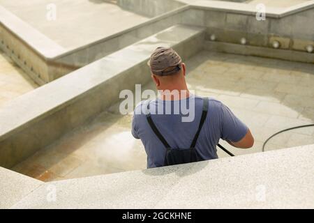 The worker washes the surface from rust. The man washes away the dirt with the help of the pressure of water. City services are cleaning the fountain. Stock Photo