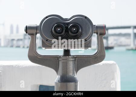 Binocular telescope mounted on a rotating base at the riverside of a modern city. Front view, close up photo with selective focus Stock Photo