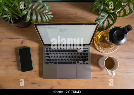 From above of opened netbook placed on wooden table with smartphone and cup of tea in workplace of freelancer Stock Photo