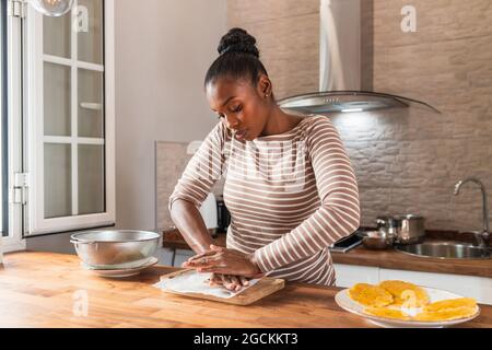 Young African American female crushing fresh plantain on cutting board while preparing patacones at home Stock Photo
