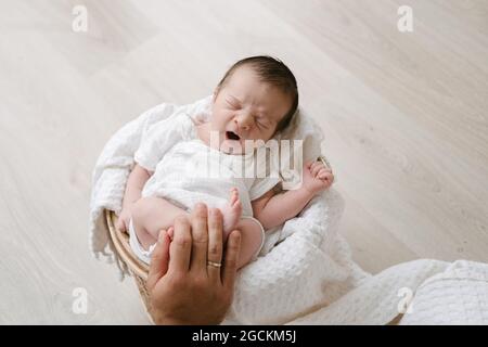 From above cropped unrecognizable hand holding adorable newborn sleeping while lying on soft blanket in basket placed on floor Stock Photo