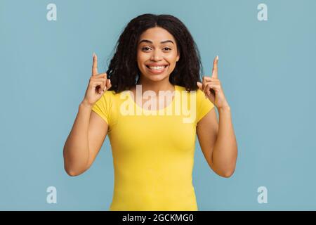 Look up. Excited african american lady pointing fingers upward showing something posing standing over blue background Stock Photo