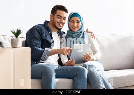 Beautiful middle-eastern couple sitting on couch with pad Stock Photo