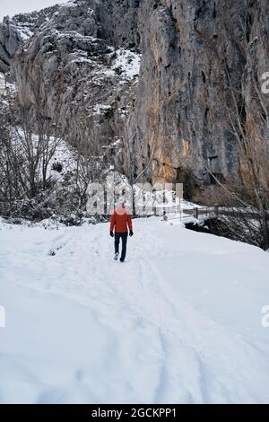 View from behind a man with red coat walking through the snowy mountains Stock Photo