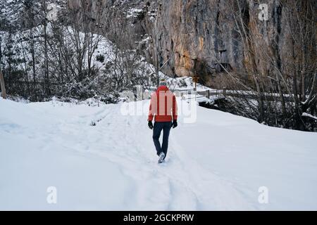 View from behind a man with red coat walking through the snowy mountains Stock Photo