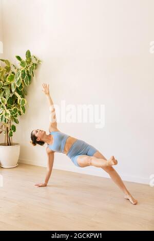 Serene female in sportswear practicing yoga in Vasishthasana while balancing on floor at home Stock Photo