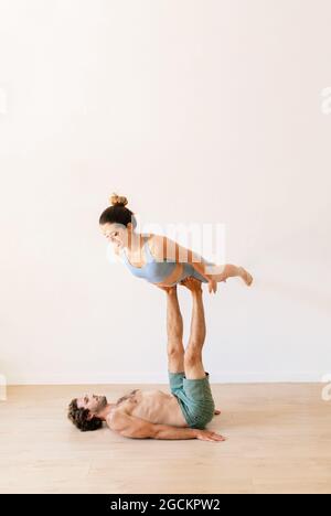 Flexible couple in activewear practicing acroyoga on floor in spacious room at home Stock Photo