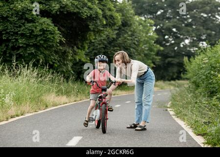 Happy Mother teaches child son to ride a bike on the bike path. Stock Photo