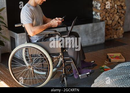 Cropped portrait of modern man with disability using laptop at home while sitting in wheelchair, copy space Stock Photo