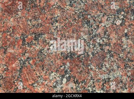 Red granite texture. A variegated, spotted background of red (brown) granite. The stone granite surface of brown-gray color. Surface view Stock Photo