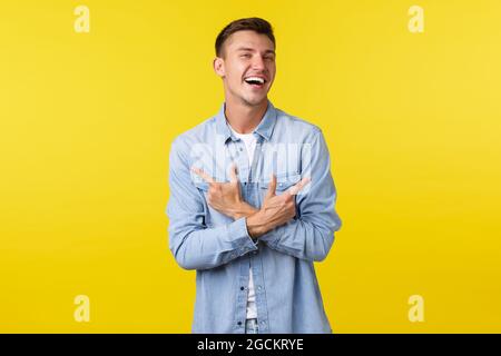 Portrait of charismatic handsome blond man laughing happy and pointing fingers sideways, showing left and right variants or products, standing Stock Photo