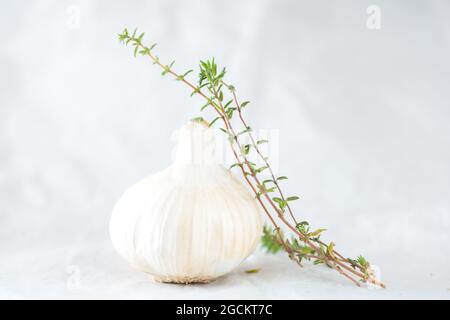 Garlic head and cloves placed with thyme on white paper on table Stock Photo