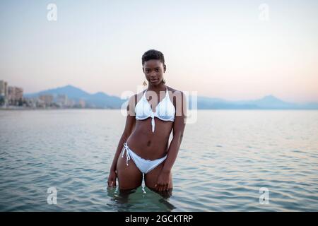 African American female in sea water looking at camera on background of sunset sky Stock Photo