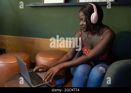 Smiling African American female freelancer in headphones browsing netbook while sitting in cafe and working on project Stock Photo