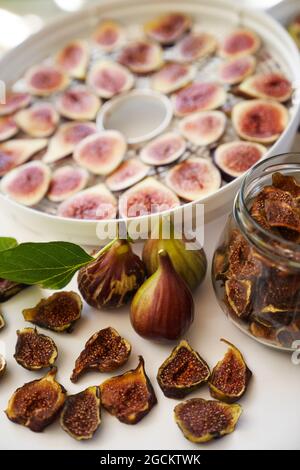 Fresh figs lie on the table next to dried figs in a glass jar and a dehydrator Stock Photo