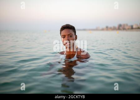 African American female in sea water looking at camera on background of sunset sky Stock Photo