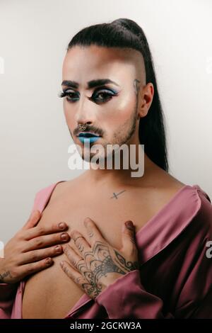 Portrait of glamorous transgender bearded Woman in sophisticated make looking at camera against neutral background Stock Photo