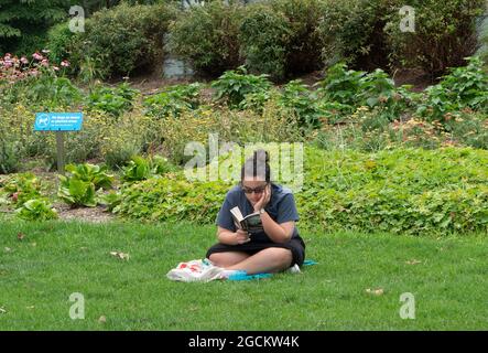 On a summer day, a woman sat in Hudson River Park reading a book. The park runs for 4.5 miles along the Hudson River on the west side of Manhattan. Stock Photo