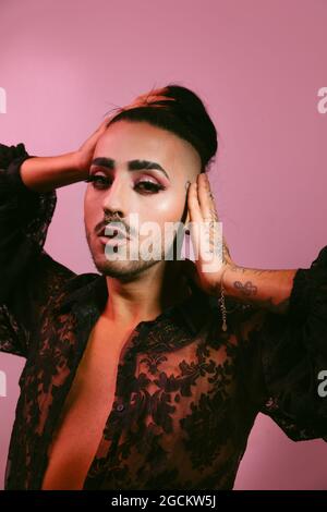 Portrait of glamorous transgender bearded Woman in sophisticated make up posing looking at camera against pink background at studio Stock Photo