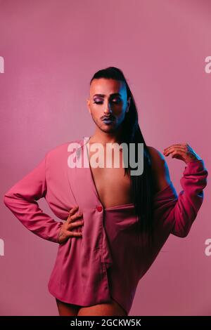 Portrait of glamorous transgender bearded Woman in sophisticated make up posing with closed eyes against pink background at studio Stock Photo