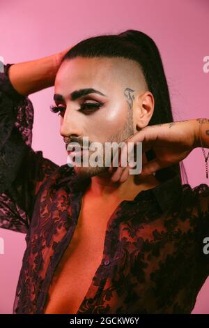 Portrait of glamorous transgender bearded Woman in sophisticated make up posing looking away against pink background at studio Stock Photo