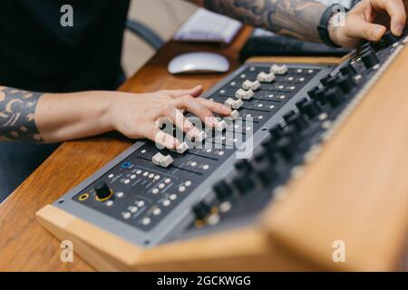 Crop unrecognizable sound man with tattoos adjusting faders on professional mixing console at table in music studio Stock Photo