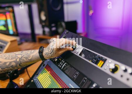 Side view of crop unrecognizable tattooed male sound engineer working with control panel on audio board in recording studio Stock Photo