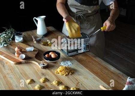 Unrecognizable person preparing raviolis and pasta at home. She is using a pasta machine Stock Photo