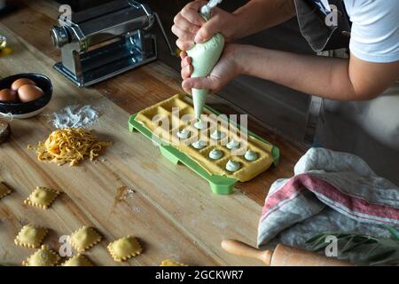 Unrecognizable person preparing raviolis and pasta at home. She is filling the ravioli with a pastry bag. Stock Photo